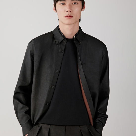 Man wearing a deep black Gambiered Canton gauze silk shirt with a relaxed straight cut and classic collar, styled with matching trousers. He moves through front, three-quarter and side views, showing the fluid drape, lightweight structure and naturally textured surface of the silk. The fabric shifts with light, revealing a subtle sheen, irregular grain and soft movement, while the clean lines, buttoned front and relaxed fit remain consistent throughout.