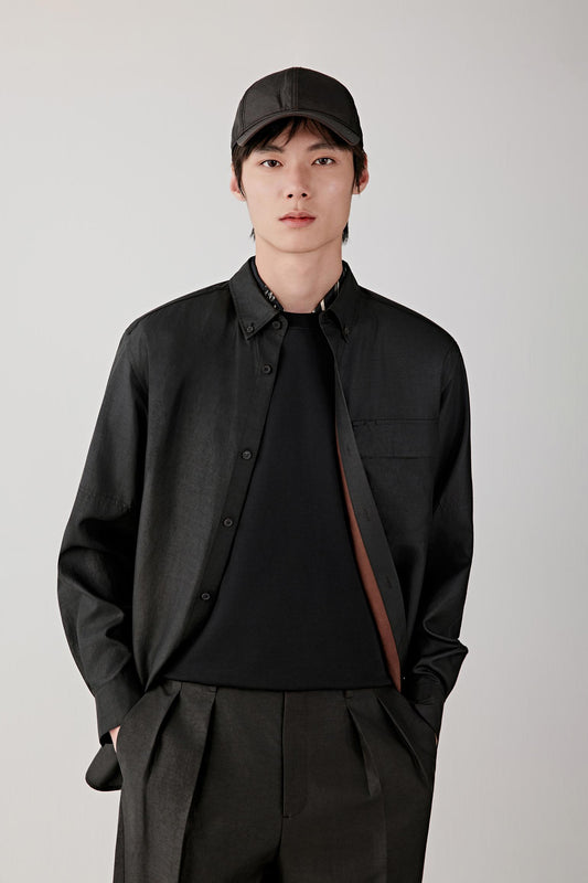 Man wearing a deep black Gambiered Canton gauze silk shirt with a relaxed straight cut and classic collar, styled with matching trousers. He moves through front, three-quarter and side views, showing the fluid drape, lightweight structure and naturally textured surface of the silk. The fabric shifts with light, revealing a subtle sheen, irregular grain and soft movement, while the clean lines, buttoned front and relaxed fit remain consistent throughout.