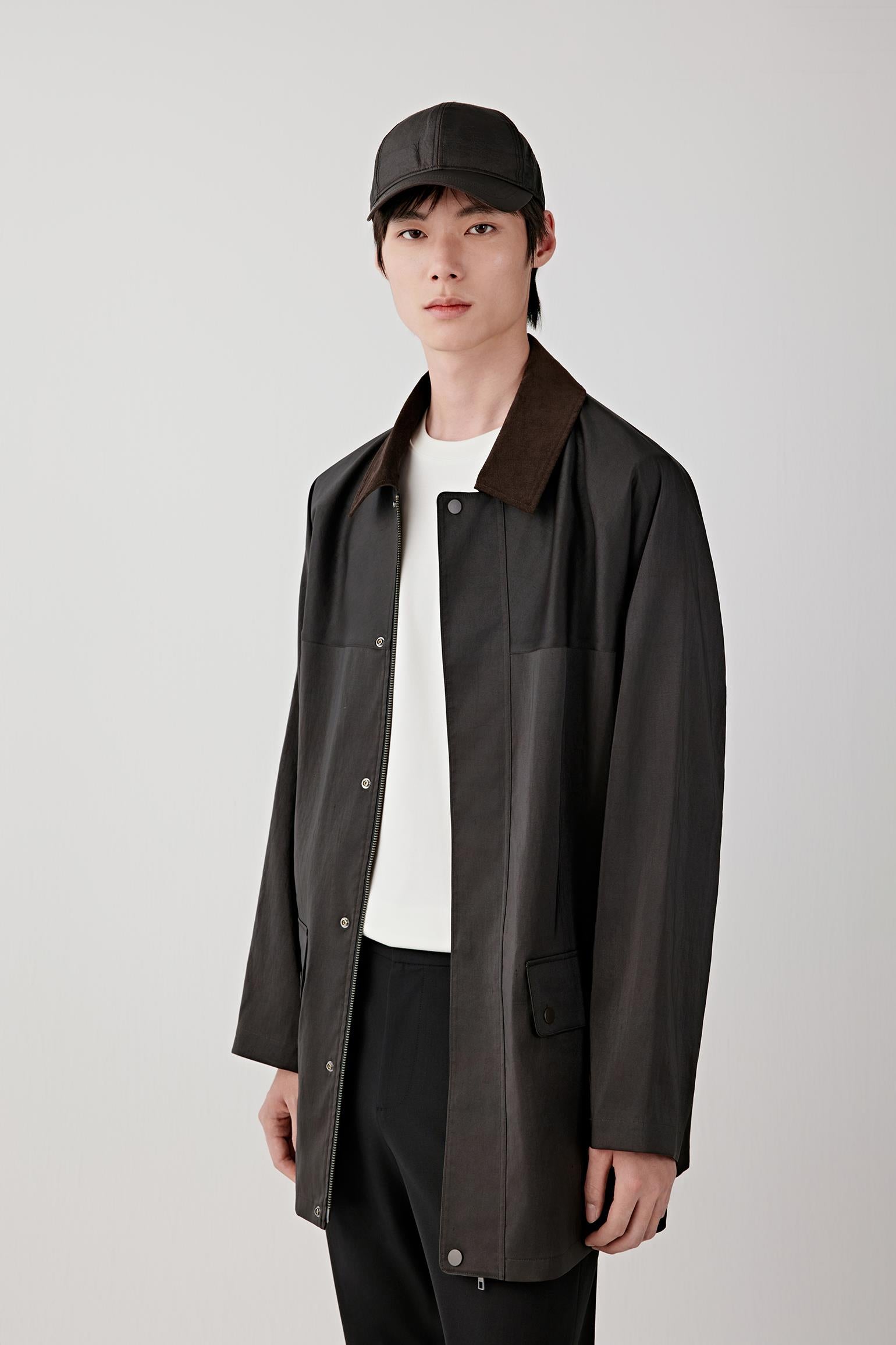 Man wearing a deep black Gambiered Canton gauze silk jacket with a straight, relaxed cut and classic collar, styled with matching trousers. He moves through front, three-quarter and side views, showing the lightweight structure, fluid drape and naturally textured surface of the silk. The fabric shifts with light, revealing a subtle sheen and depth from the dyeing process, while the clean lines, concealed fastening and relaxed fit remain consistent throughout.