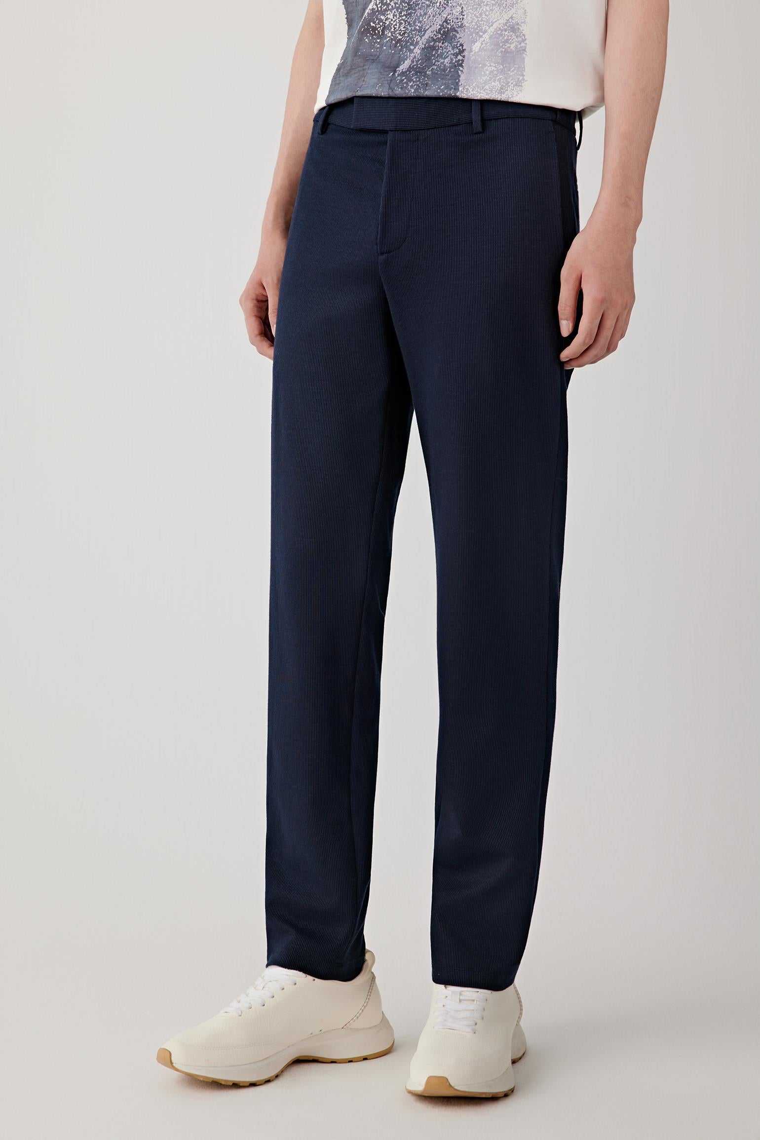 Man wearing navy ramie cotton and jacquard jersey trousers with a straight-leg cut and mid-rise waist, styled with a white T-shirt and cap. He moves through front, side and slight turning views, showing the clean vertical line, lightweight structure and soft drape of the fabric. The trousers fall straight from the hips with a natural, fluid movement, highlighting the subtle textured surface, comfortable fit and ease of motion.