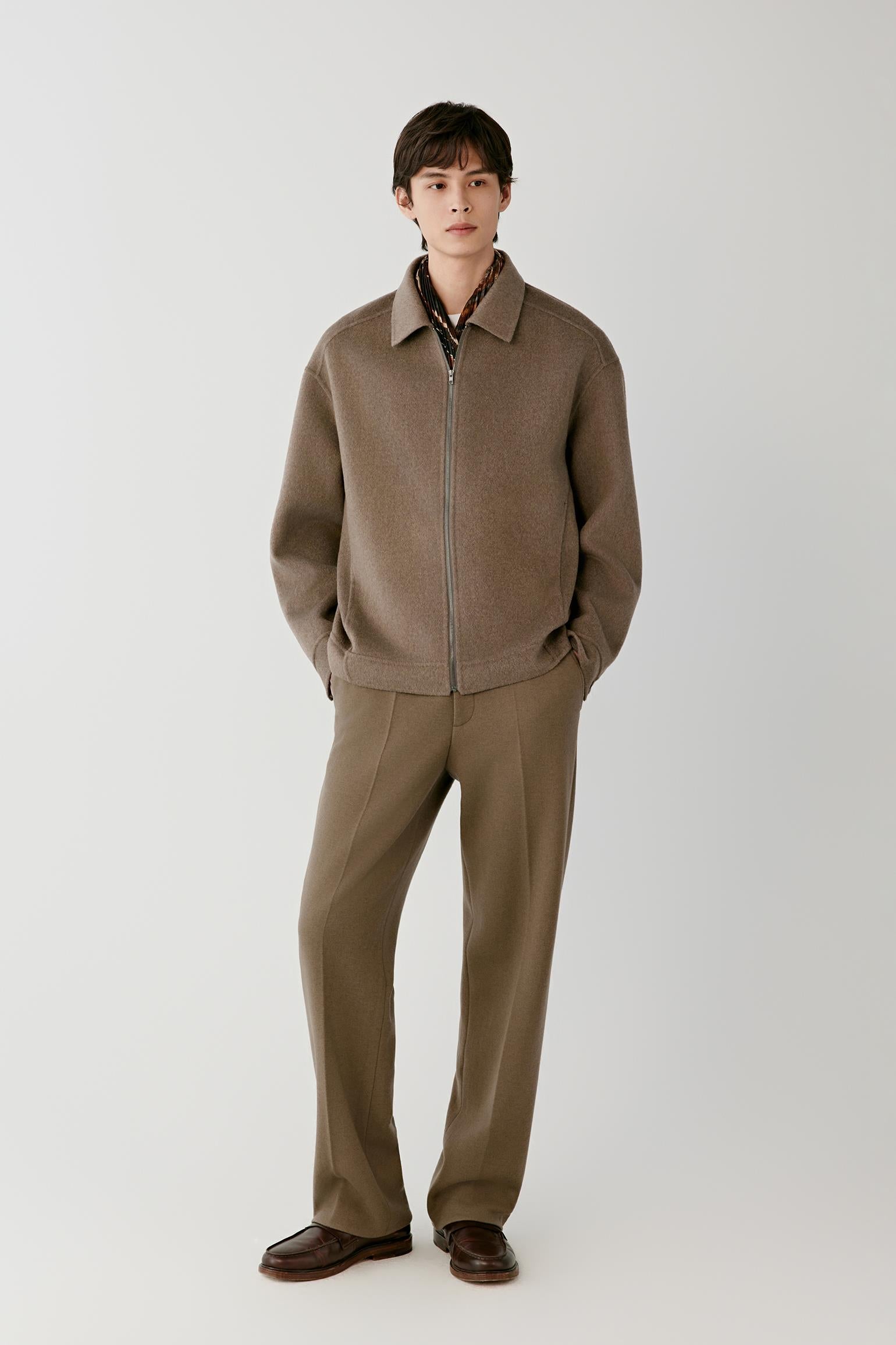 Video Front view of a man wearing a brown melange cashmere jacket, showing the relaxed silhouette, pointed collar and front zip fastening.