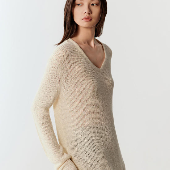 Woman wearing an ivory spun silk knit pullover with a relaxed, fluid fit, styled with a long black skirt. She moves through front and side views, showing the lightweight open-knit texture, soft drape and slight transparency. The round neckline, long sleeves and natural texture remain visible, while the fabric follows the body gently, emphasizing breathability and ease of movement.