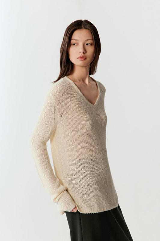 Woman wearing an ivory spun silk knit pullover with a relaxed, fluid fit, styled with a long black skirt. She moves through front and side views, showing the lightweight open-knit texture, soft drape and slight transparency. The round neckline, long sleeves and natural texture remain visible, while the fabric follows the body gently, emphasizing breathability and ease of movement.