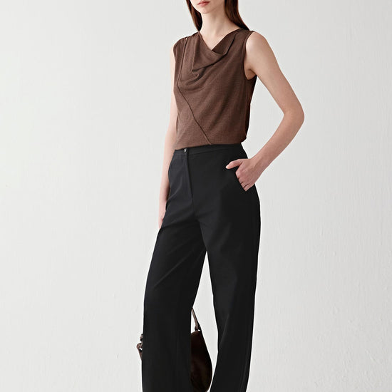 Video showing a woman wearing a dark brown draped top in tussah silk, moving to reveal the fluid drape and softly textured knit surface. The fabric follows the movement of the body with a supple, continuous flow, while the draped neckline and diagonal wrap seam create layered folds across the front. The sleeveless construction and bound edges remain defined as the lightweight knit shifts naturally, highlighting the subtle sheen, textured surface and fluid silhouette.