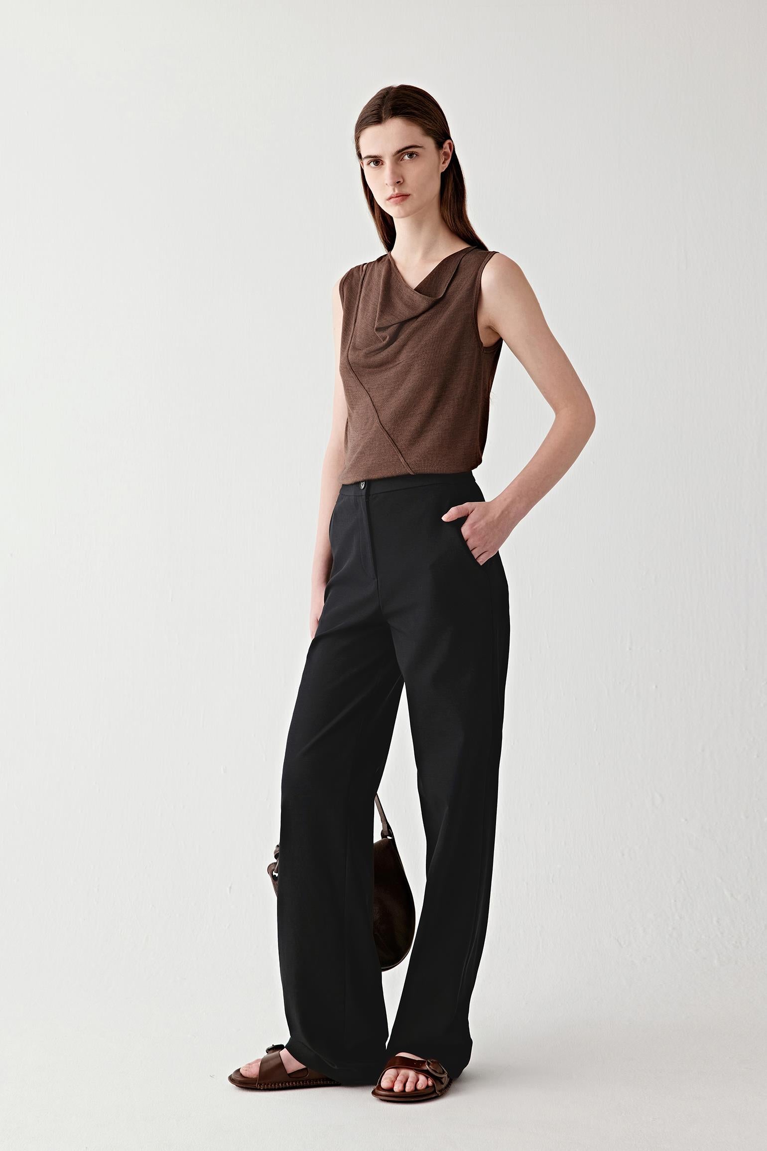 Video showing a woman wearing a dark brown draped top in tussah silk, moving to reveal the fluid drape and softly textured knit surface. The fabric follows the movement of the body with a supple, continuous flow, while the draped neckline and diagonal wrap seam create layered folds across the front. The sleeveless construction and bound edges remain defined as the lightweight knit shifts naturally, highlighting the subtle sheen, textured surface and fluid silhouette.