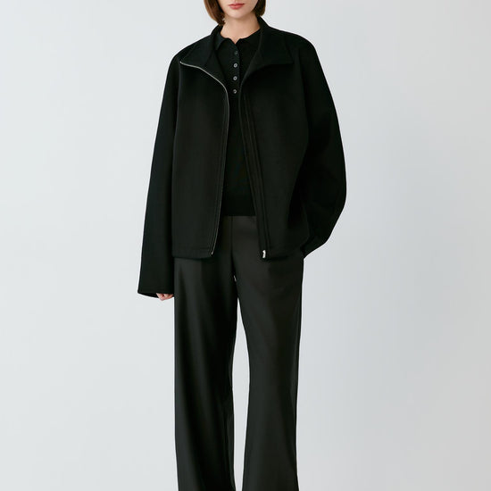 Video of a woman wearing a black double-faced cashmere jacket, showing the movement of the rounded silhouette and wide sleeves as she moves.