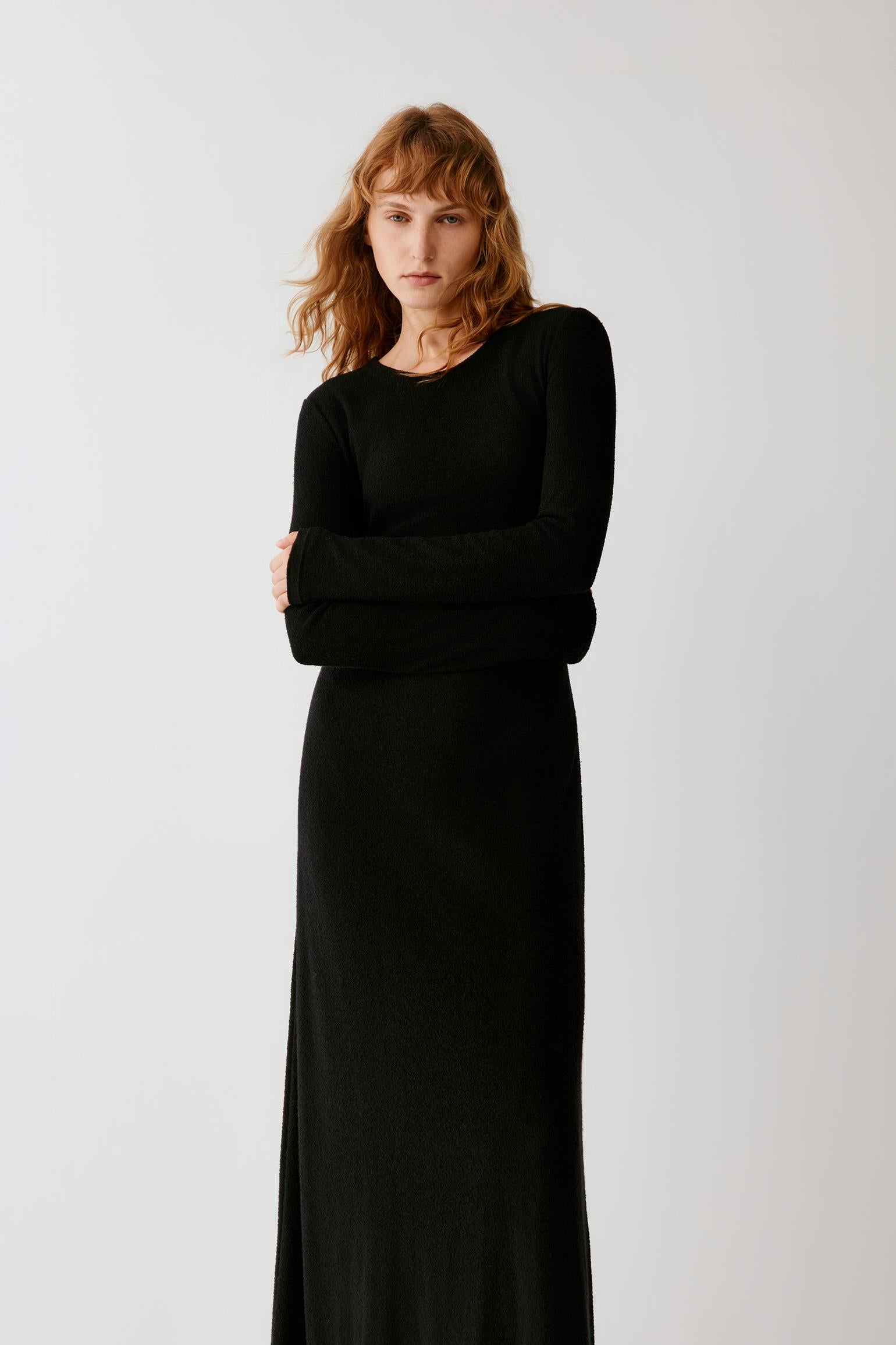 Woman wearing a long black fitted dress with long sleeves and black loafers.