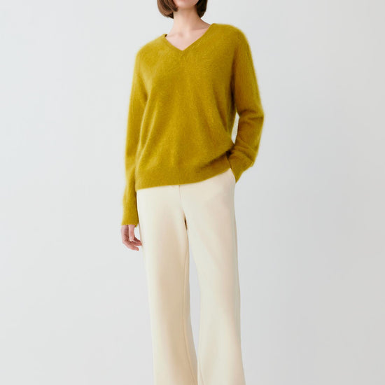 Video Front view of a woman wearing a mustard yellow cashmere pullover, showing the V-neck, long sleeves and straight silhouette.