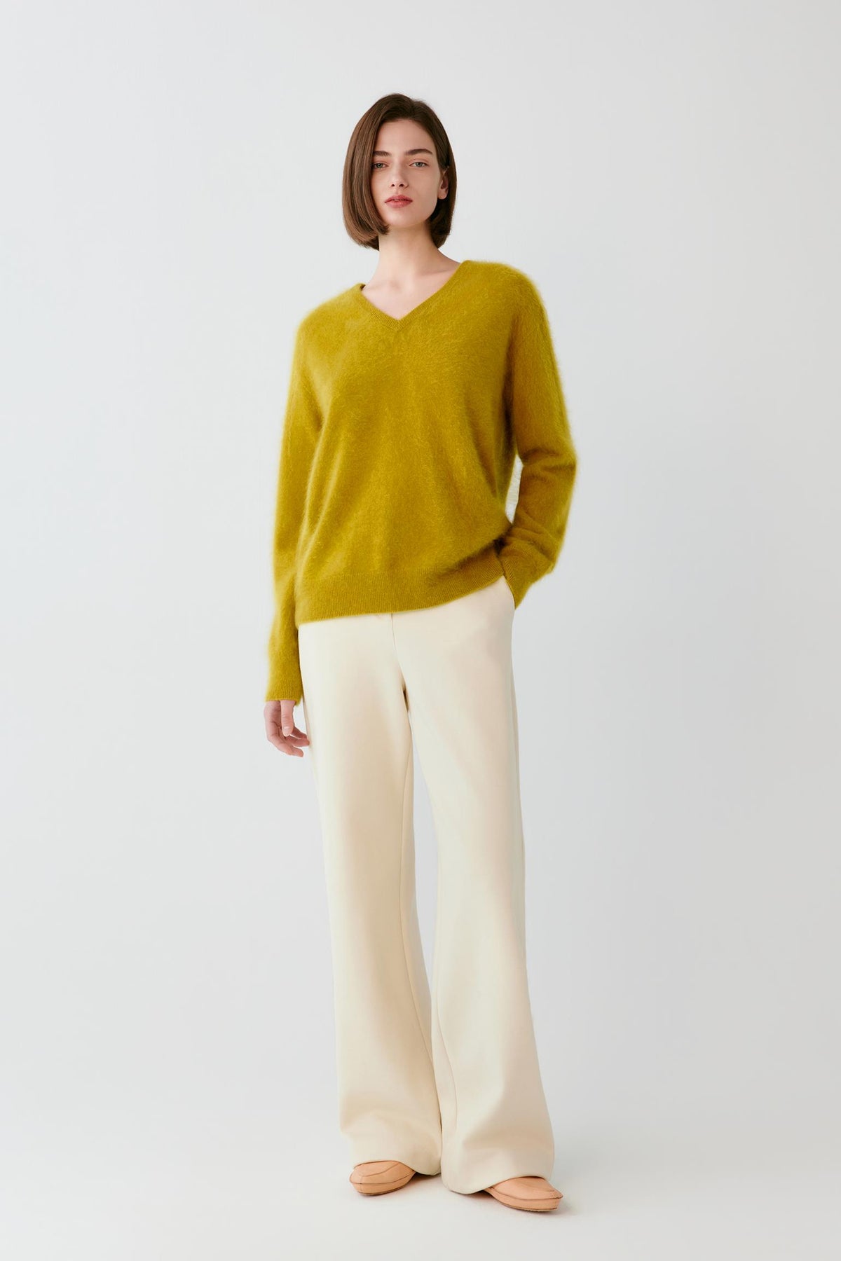 Video Front view of a woman wearing a mustard yellow cashmere pullover, showing the V-neck, long sleeves and straight silhouette.