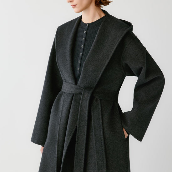 Video of a woman wearing a dark grey melange double-face wool and cashmere coat, showing the wide shawl collar, self-tie belt and long silhouette.