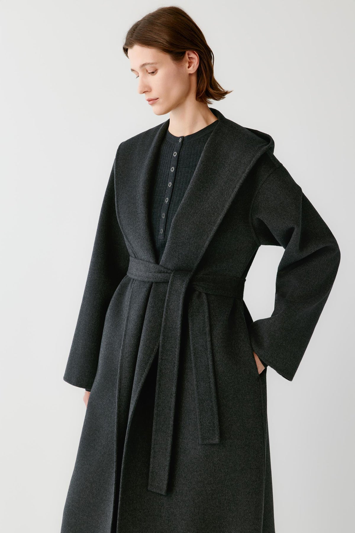 Video of a woman wearing a dark grey melange double-face wool and cashmere coat, showing the wide shawl collar, self-tie belt and long silhouette.