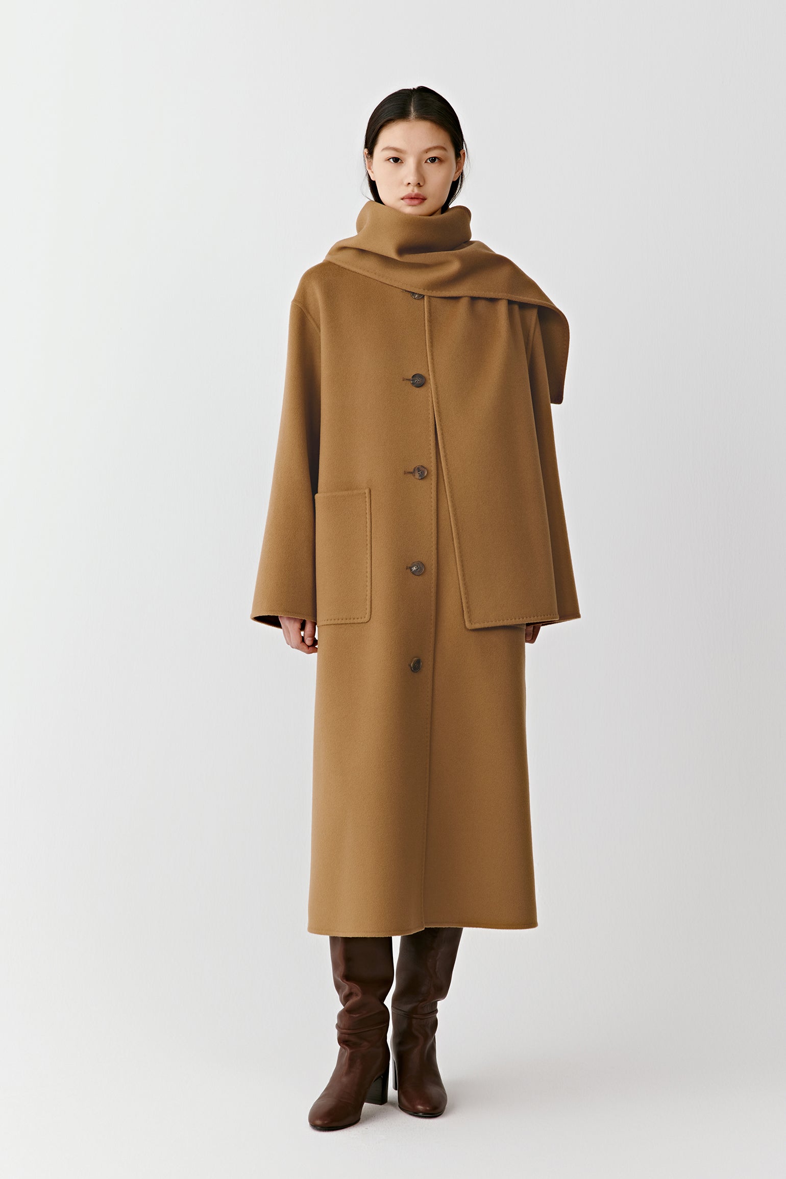 Product video showing a camel straight coat in double-faced wool and cashmere with an integrated scarf, rotating to display the fit, length, scarf detail, pockets, and overall silhouette from all angles.