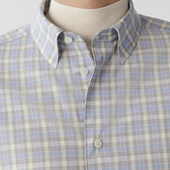 Video Front view of a man wearing a light blue, grey and white checked worsted wool shirt, showing the classic collar, button-front fastening and straight hem.