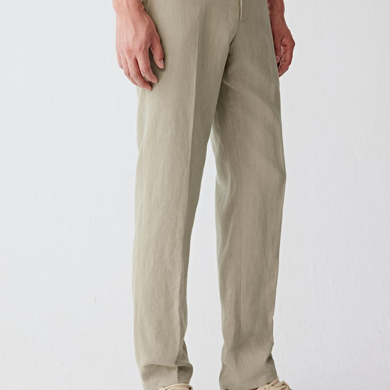 Man wearing natural beige linen trousers with a straight cut and front crease, styled with a matching lightweight jacket. He moves through front, side and angled views, showing the breathable linen fabric, dry hand feel and softly textured surface. The clean waistband, discreet pockets and straight leg line remain visible, while the material moves naturally with the body, emphasizing lightness, ventilation and ease of movement in warm conditions.