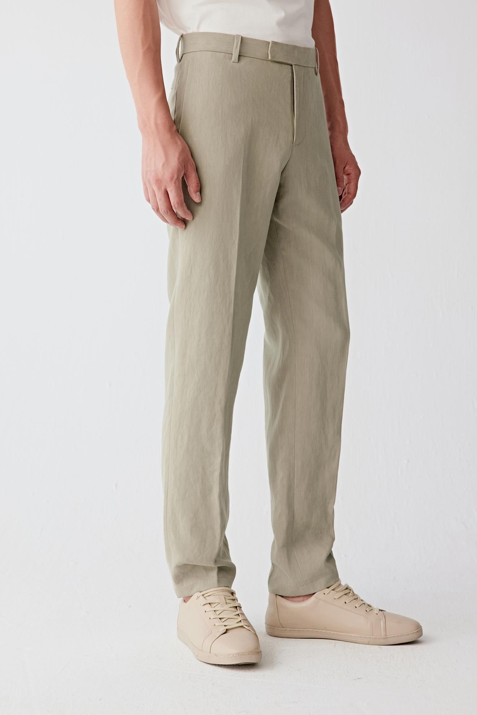 Man wearing natural beige linen trousers with a straight cut and front crease, styled with a matching lightweight jacket. He moves through front, side and angled views, showing the breathable linen fabric, dry hand feel and softly textured surface. The clean waistband, discreet pockets and straight leg line remain visible, while the material moves naturally with the body, emphasizing lightness, ventilation and ease of movement in warm conditions.