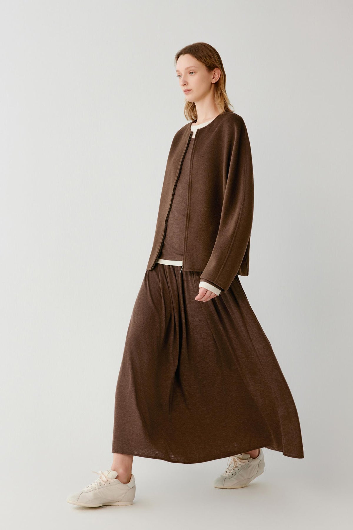 Video of a woman wearing a dark brown sleeveless coat in double-face yak and wool, showing the fluid movement of the long silhouette and the natural drape of the fabric as she walks.