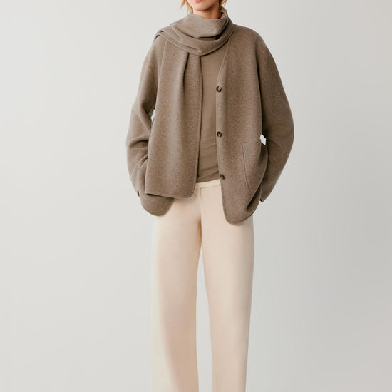 Video of a woman wearing a taupe wool and cashmere blend jersey coat, showing the fluid movement of the relaxed silhouette and integrated scarf as she moves.