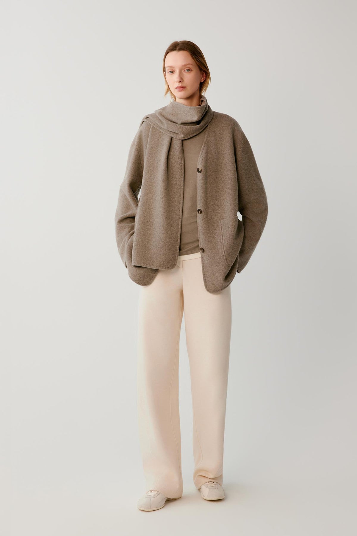 Video of a woman wearing a taupe wool and cashmere blend jersey coat, showing the fluid movement of the relaxed silhouette and integrated scarf as she moves.