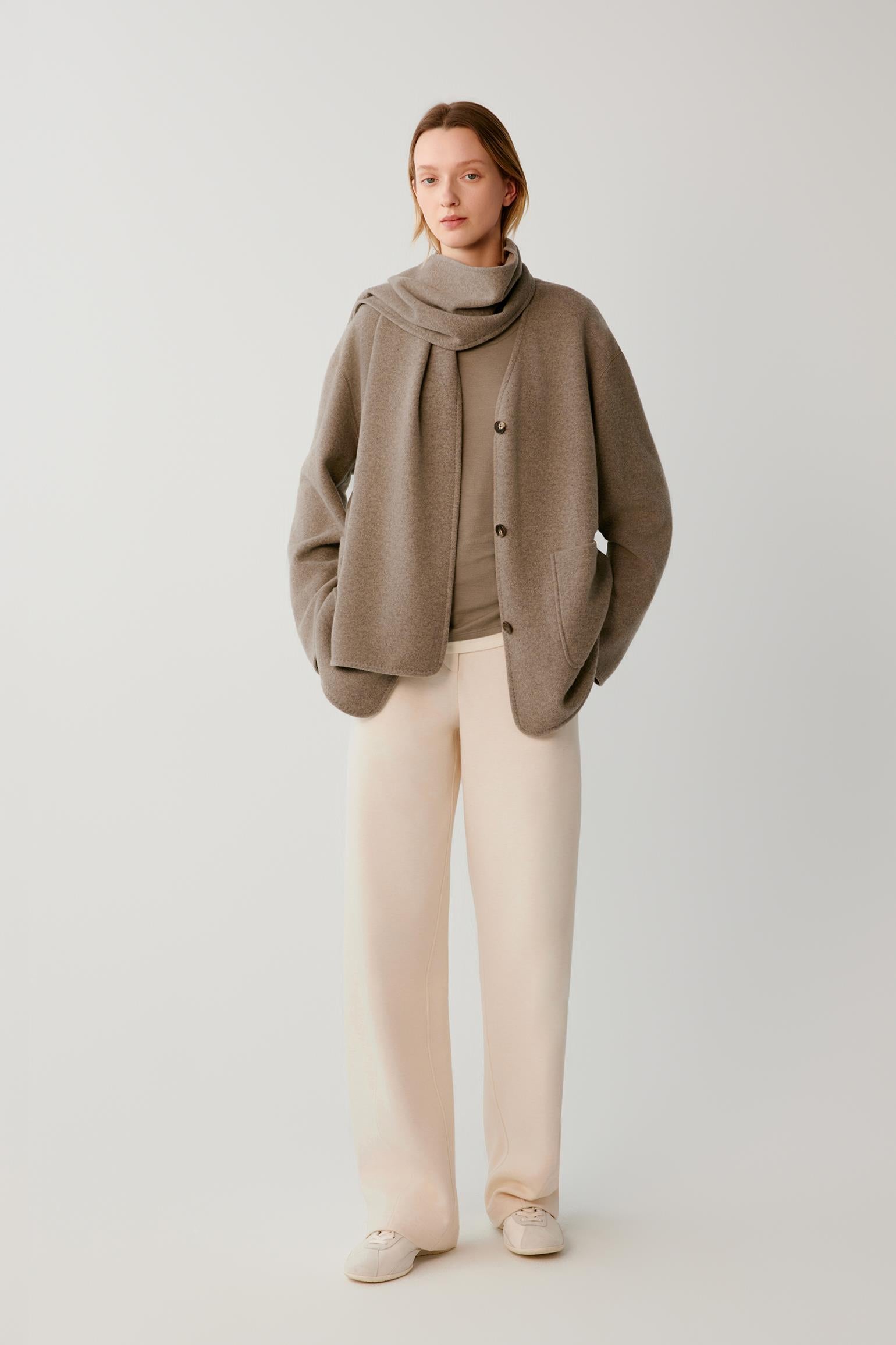 Video of a woman wearing a taupe wool and cashmere blend jersey coat, showing the fluid movement of the relaxed silhouette and integrated scarf as she moves.