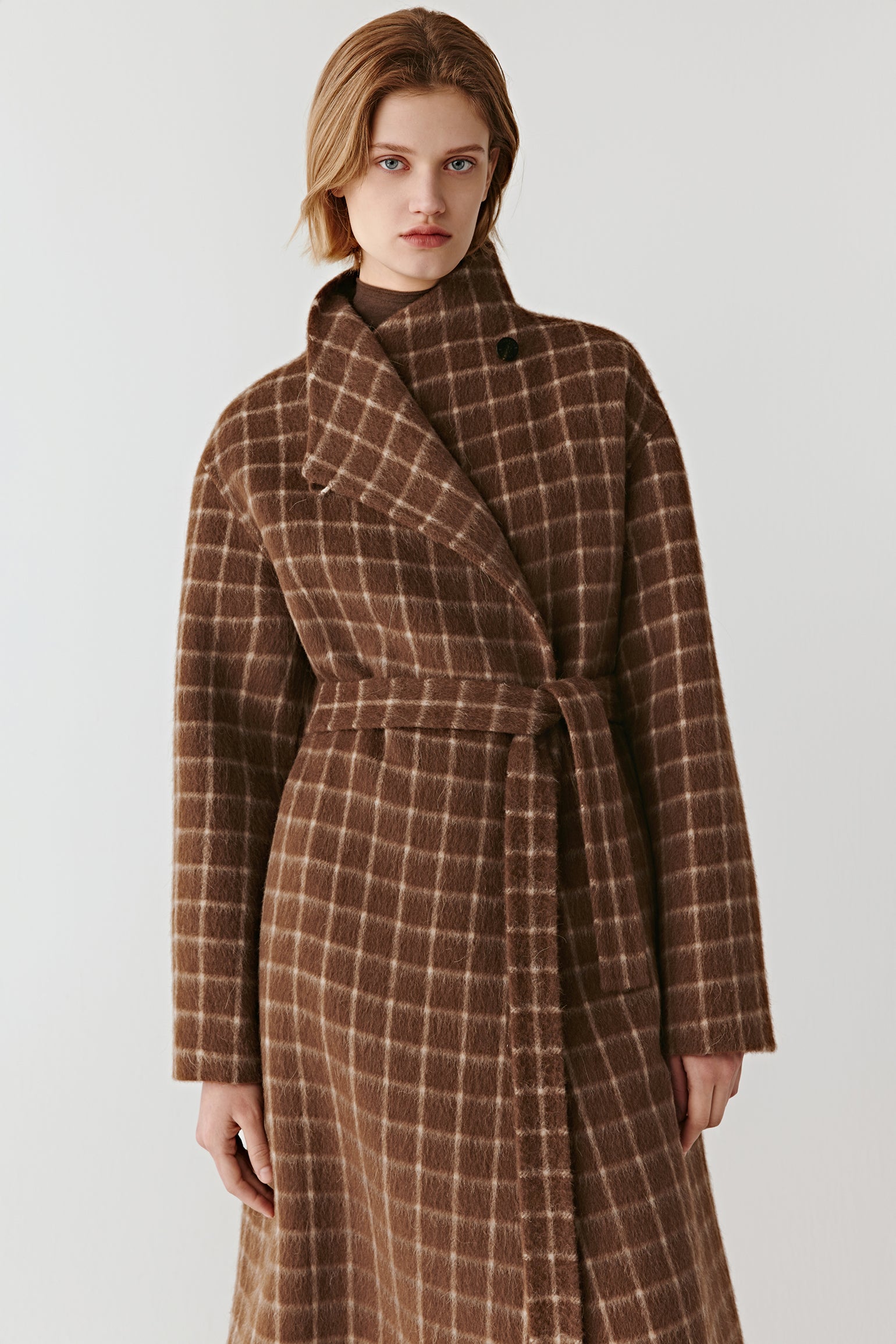 Product video showing a double-faced checked wool coat in natural brown tones, rotating to display the check pattern, collarless round neckline, raglan sleeves, welt pockets, and overall silhouette from all angles.