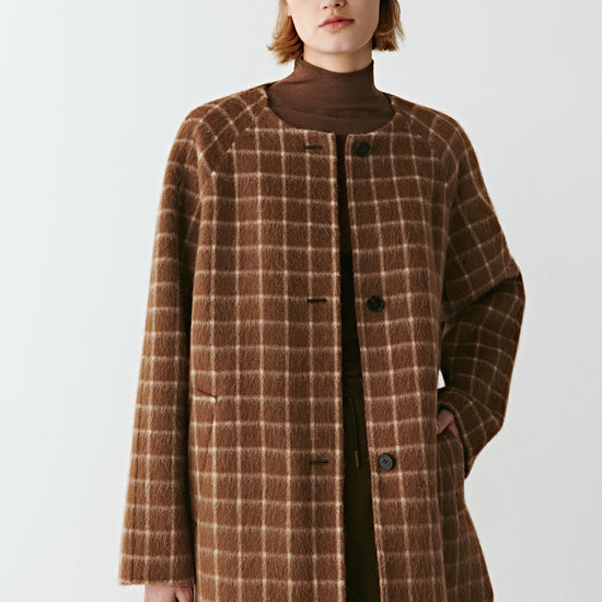 Product video showing a short double-faced checked wool coat in natural brown tones, rotating to display the check pattern, collarless round neckline, raglan sleeves, welt pockets, and overall silhouette from all angles.