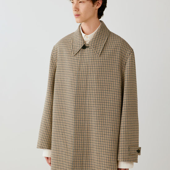 Video of a man wearing a beige and black houndstooth wool coat, showing the movement of the long silhouette and structured fabric as he walks.