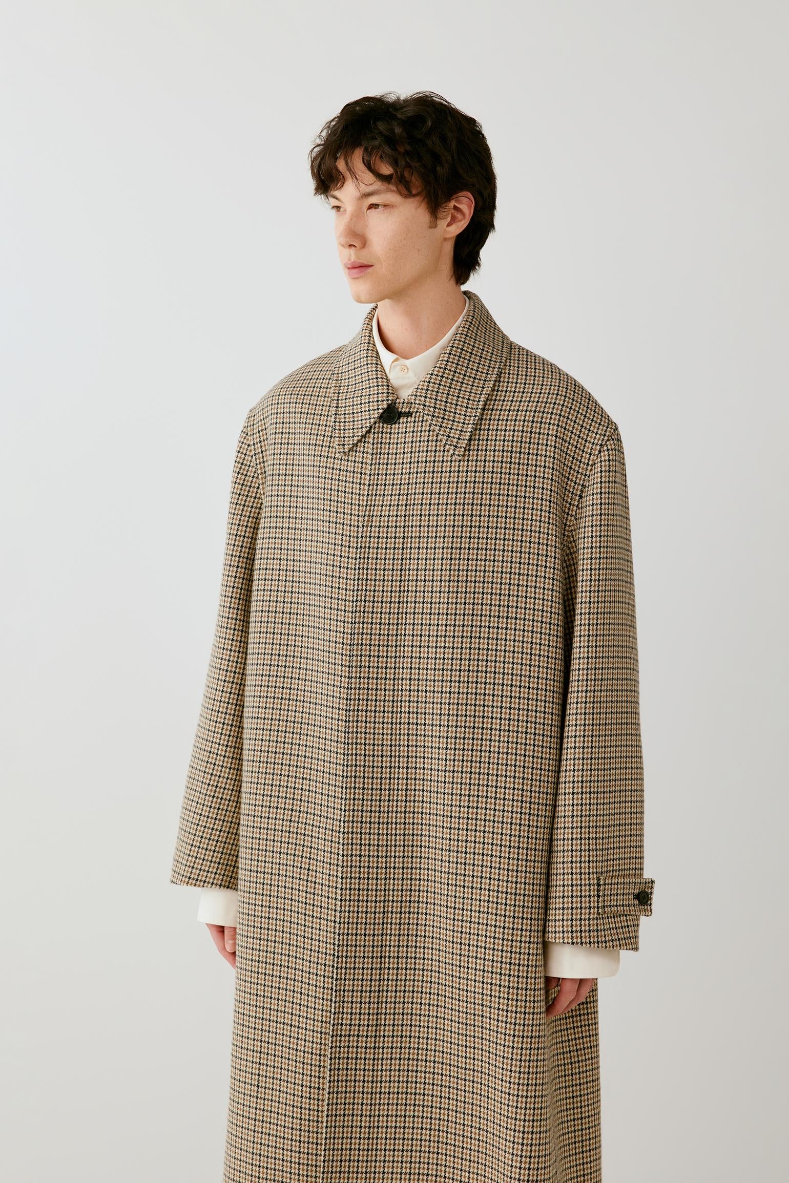 Video of a man wearing a beige and black houndstooth wool coat, showing the movement of the long silhouette and structured fabric as he walks.