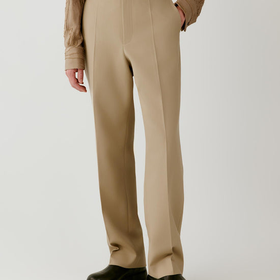 Video of a man wearing beige wool twill trousers, showing the movement of the straight-leg silhouette and structured drape as he walks.