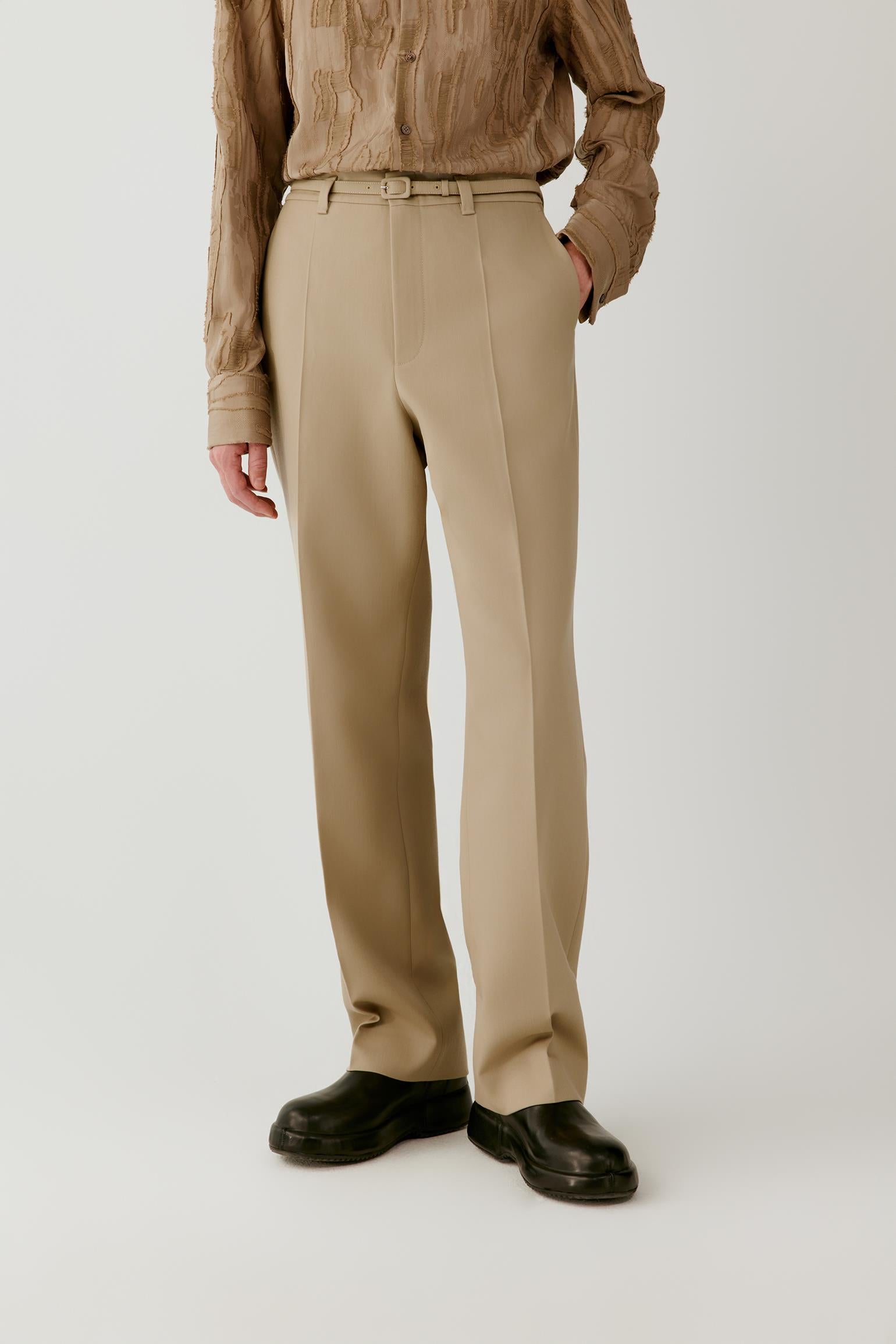 Video of a man wearing beige wool twill trousers, showing the movement of the straight-leg silhouette and structured drape as he walks.