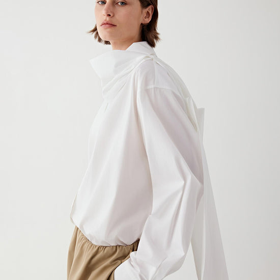 Video of a woman wearing the white cotton poplin shirt while turning slightly in a studio setting. The movement shows the fluid drape of the lightweight cotton fabric, the relaxed silhouette of the shirt and the way the long sleeves and hem move naturally with the body.