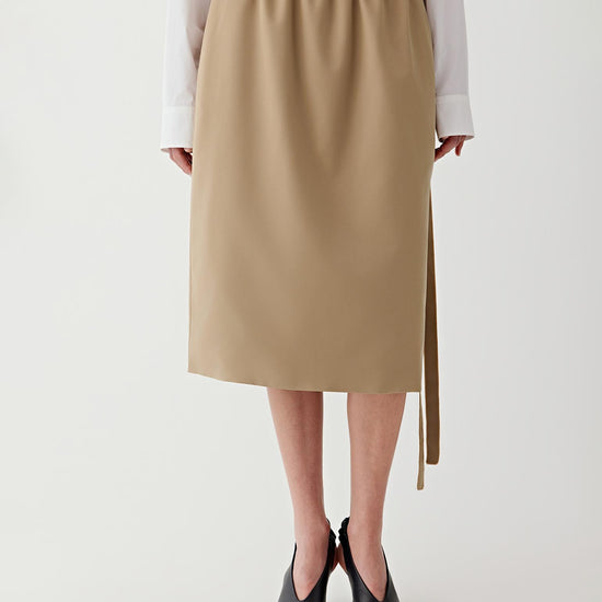 Woman wearing a beige skirt with a white shirt on a plain background