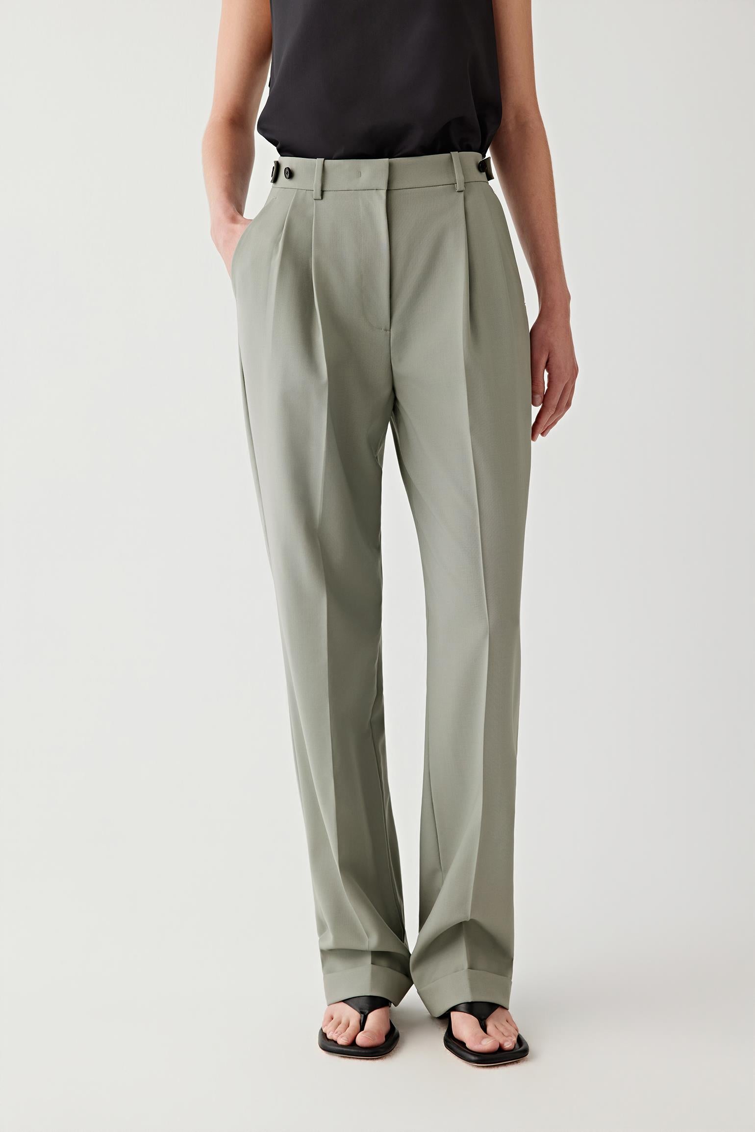 Person wearing light gray pleated pants on a white background