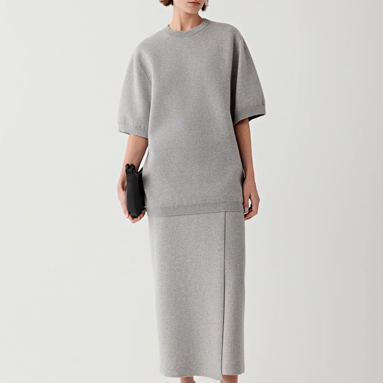 Video showing the model wearing the melange grey wool and cashmere pullover in motion. The footage highlights the relaxed silhouette of the sweater, the generous elbow-length sleeves and the fluid drape of the knit fabric across the body. As the model walks, the melange knit surface reveals subtle tonal variations.