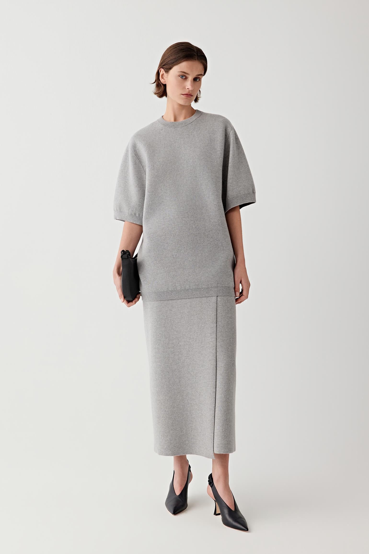 Video showing the model wearing the melange grey wool and cashmere pullover in motion. The footage highlights the relaxed silhouette of the sweater, the generous elbow-length sleeves and the fluid drape of the knit fabric across the body. As the model walks, the melange knit surface reveals subtle tonal variations.