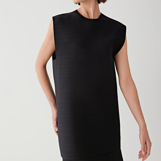 Woman wearing a black sleeveless top with black skirt against a plain background