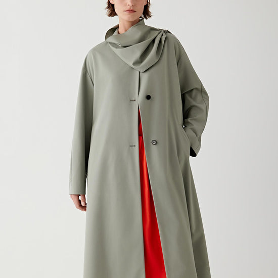 Woman wearing a long olive green coat over a red dress on a white 