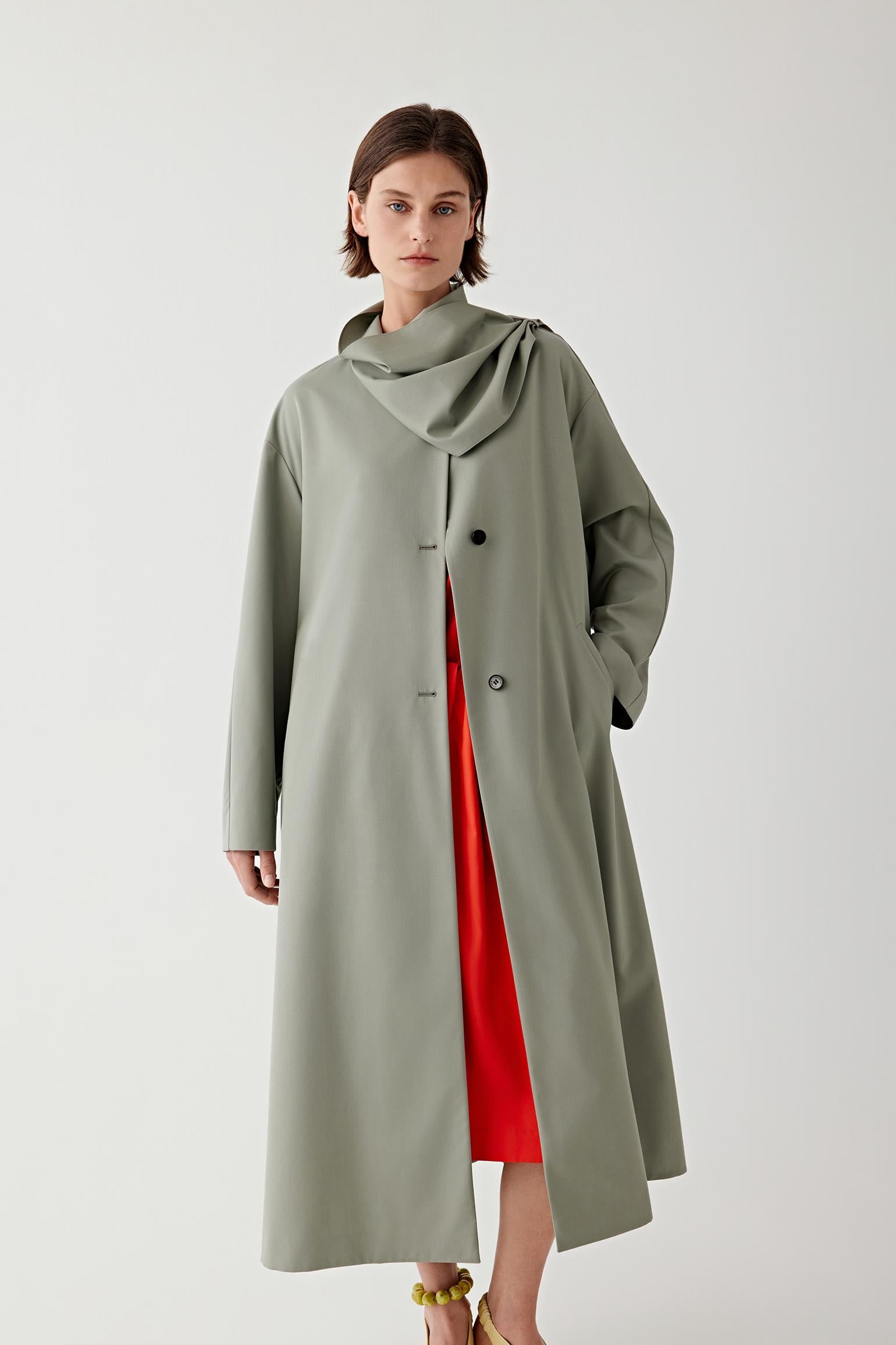 Woman wearing a long olive green coat over a red dress on a white 