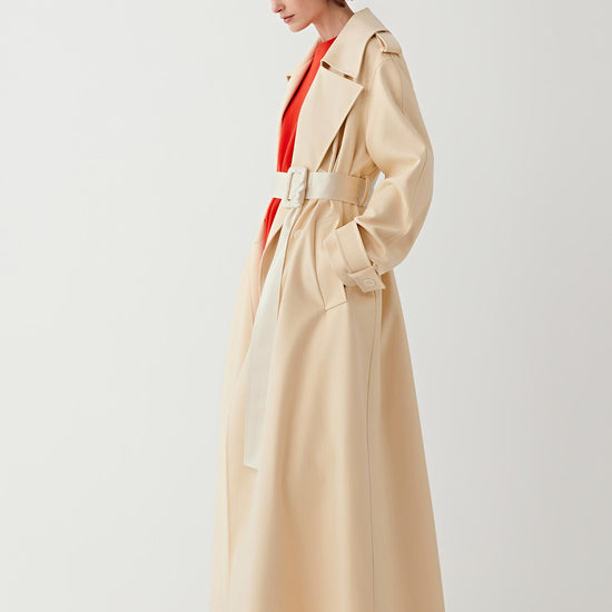 Woman wearing a beige trench coat over a red outfit on a white 
