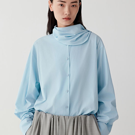 Video showing the model turning while wearing the light blue shirt, revealing the soft movement of the cotton poplin fabric and the sculptural fold of the collar.