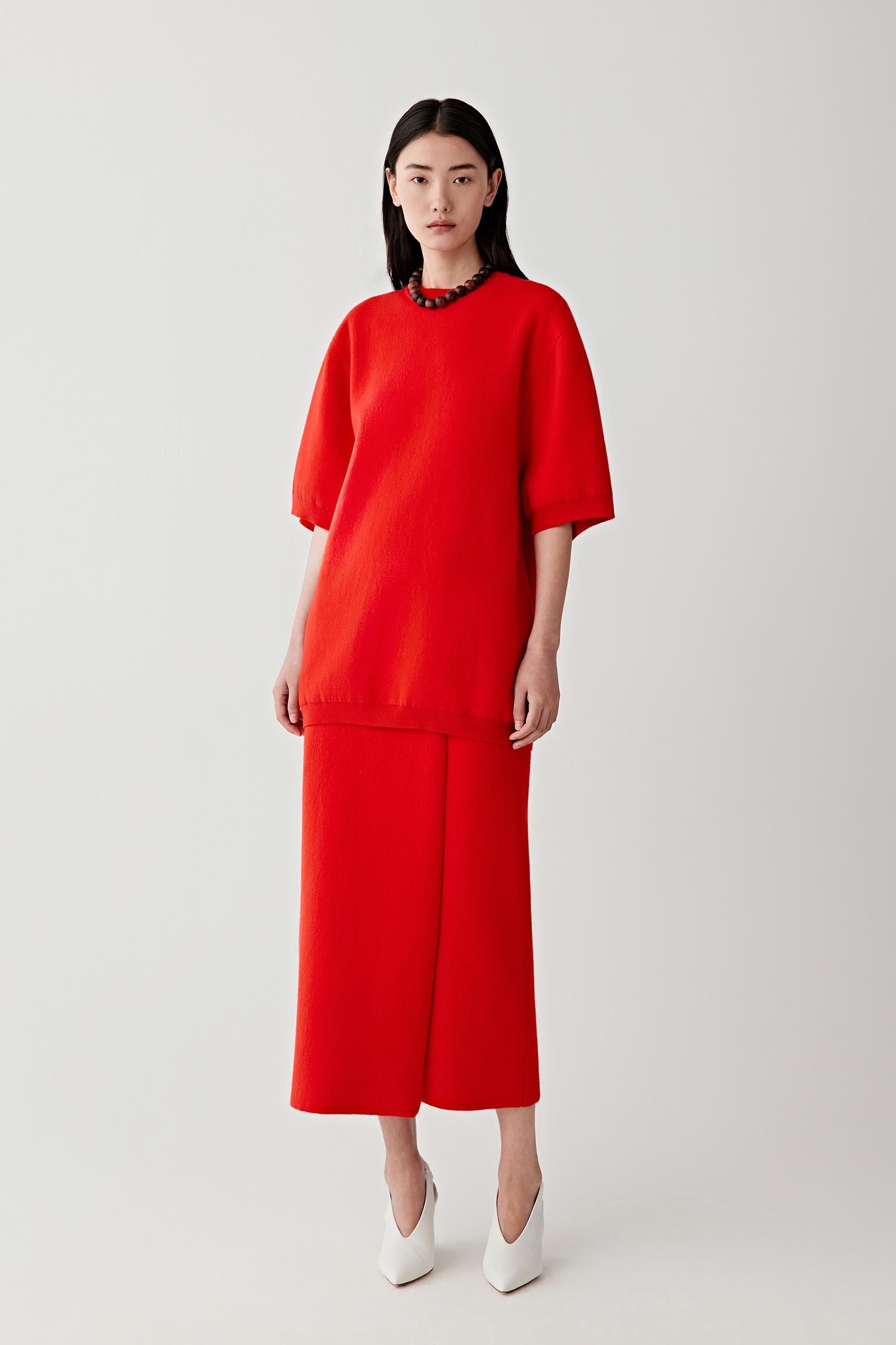 Video showing the model wearing the bright red pullover knitted from wool and cashmere while moving in the studio. The footage highlights the bold colour of the garment, the relaxed silhouette and the wide short sleeves that create a fluid shape. The lightweight knit drapes naturally across the torso while maintaining a clean structure.