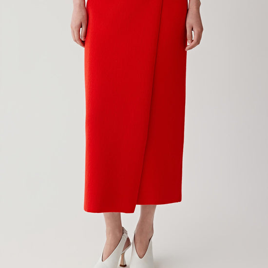 Video showing the model walking and turning while wearing the wool and cashmere skirt in intense red. The movement reveals the structured knit fabric and the steady drape of the garment as it moves with the body. The straight silhouette remains clean and balanced while the dense knit maintains its shape. The vibrant red tone stands out clearly as the fabric shifts with each step.