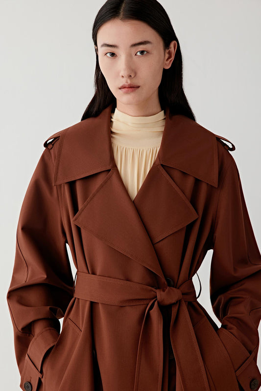 Woman wearing a long brown coat against a white background