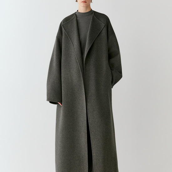 Video of a woman wearing a grey melange double-face wool coat, showing the movement of the long silhouette and fluid drape as she walks.