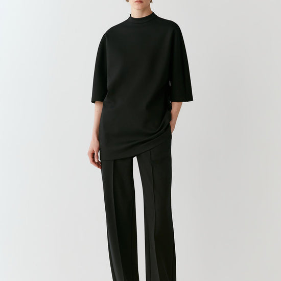 Video of a woman wearing a deep black wool T-shirt, showing the elongated relaxed silhouette and movement of the Ponte di Roma jersey as she moves.