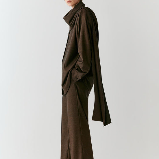 Video of a woman wearing a brown melange wool flannel shirt, showing the movement of the long silhouette and integrated scarf panel as she moves.