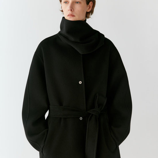 Video of a woman wearing a black wool double-face coat, showing the movement of the short silhouette, wide sleeves and self-tie belt as she moves.
