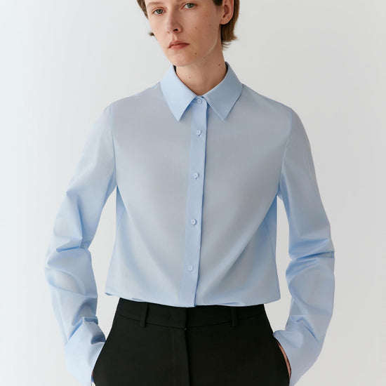 Video of a woman wearing a light blue cotton poplin shirt, showing the movement of the relaxed silhouette and structured fabric as she moves.