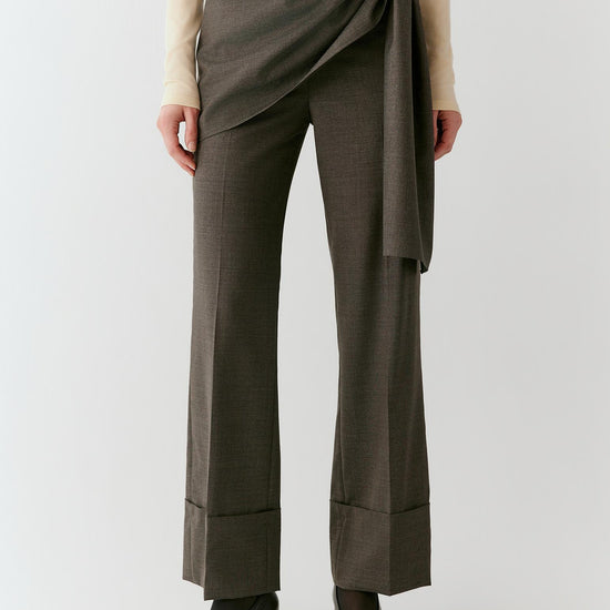 Video of a woman wearing grey melange wool trousers, showing the movement of the straight-leg silhouette and asymmetric wrap-front panel as she walks.