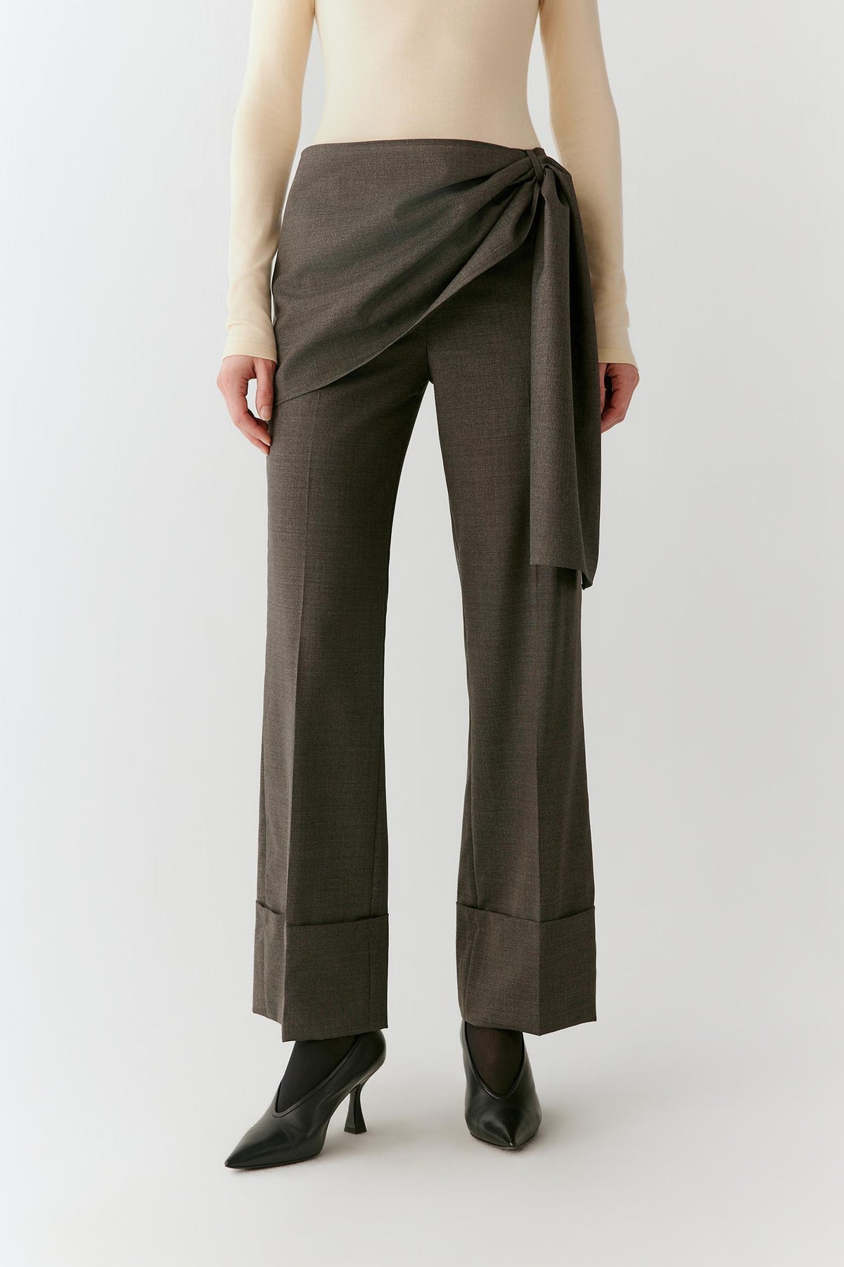 Video of a woman wearing grey melange wool trousers, showing the movement of the straight-leg silhouette and asymmetric wrap-front panel as she walks.
