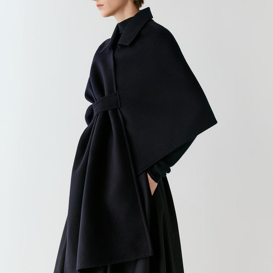 Video of a woman wearing a deep black wool and silk cape, showing the movement of the asymmetric silhouette and fluid drape as she moves.